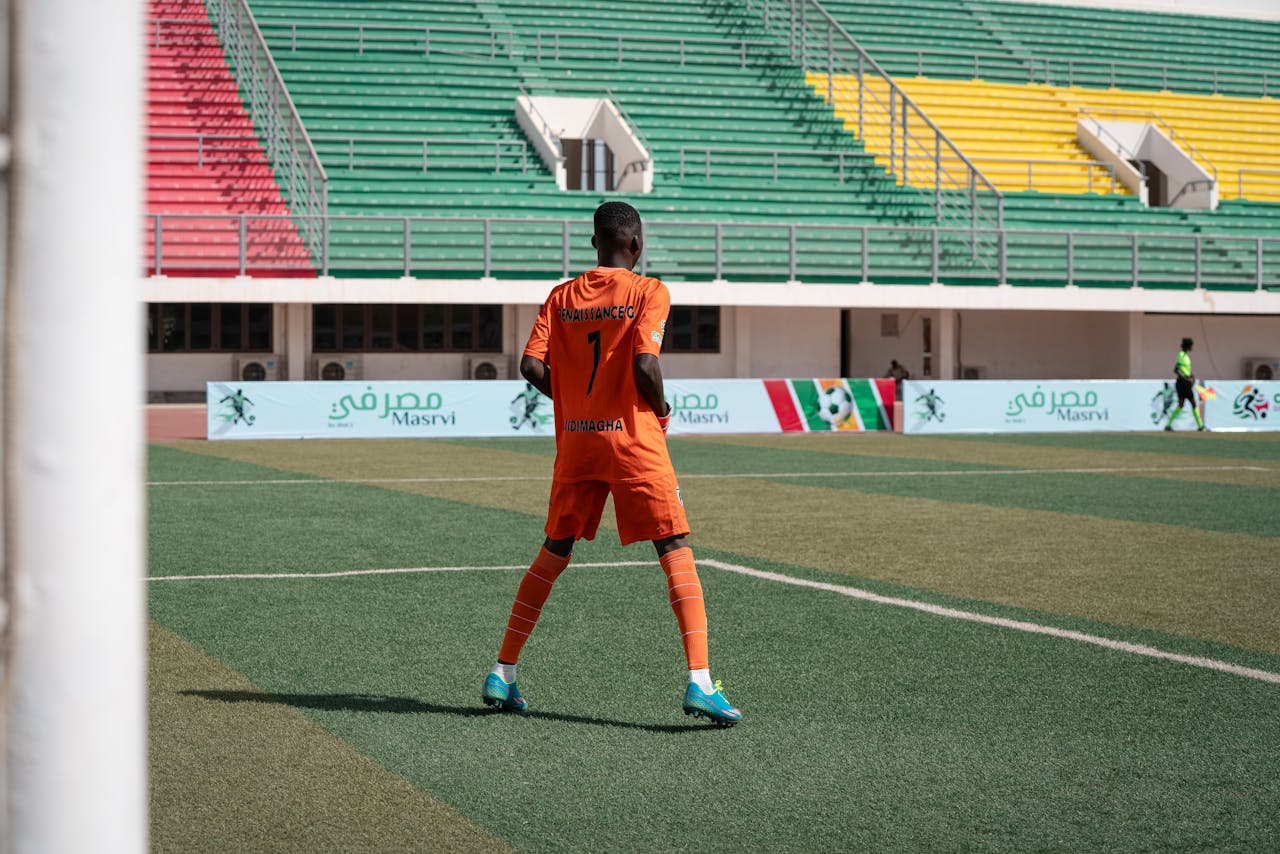 services-01 Soccer player in orange uniform on colorful stadium field during daytime game.