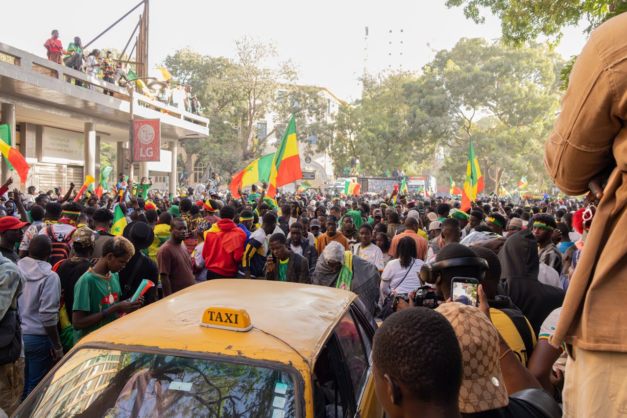 services-03 A lively street scene in Dakar, Senegal, with a crowd celebrating and waving flags.